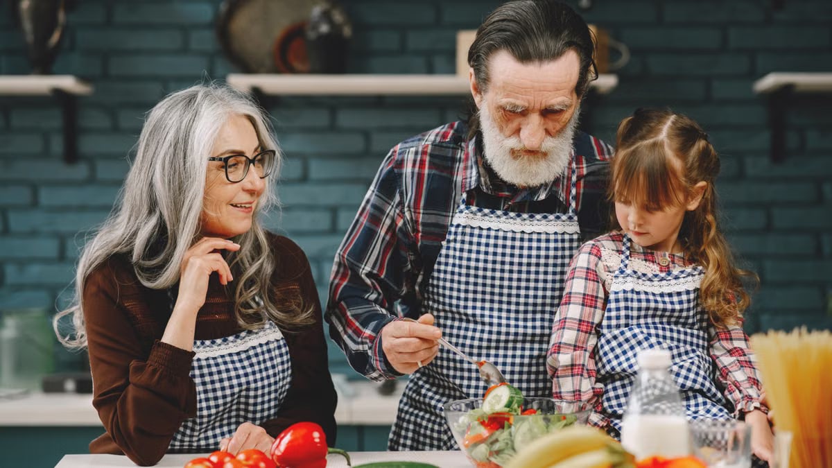 Grandparents and granddaughter preparing salad in home kitchen, creating memories together.